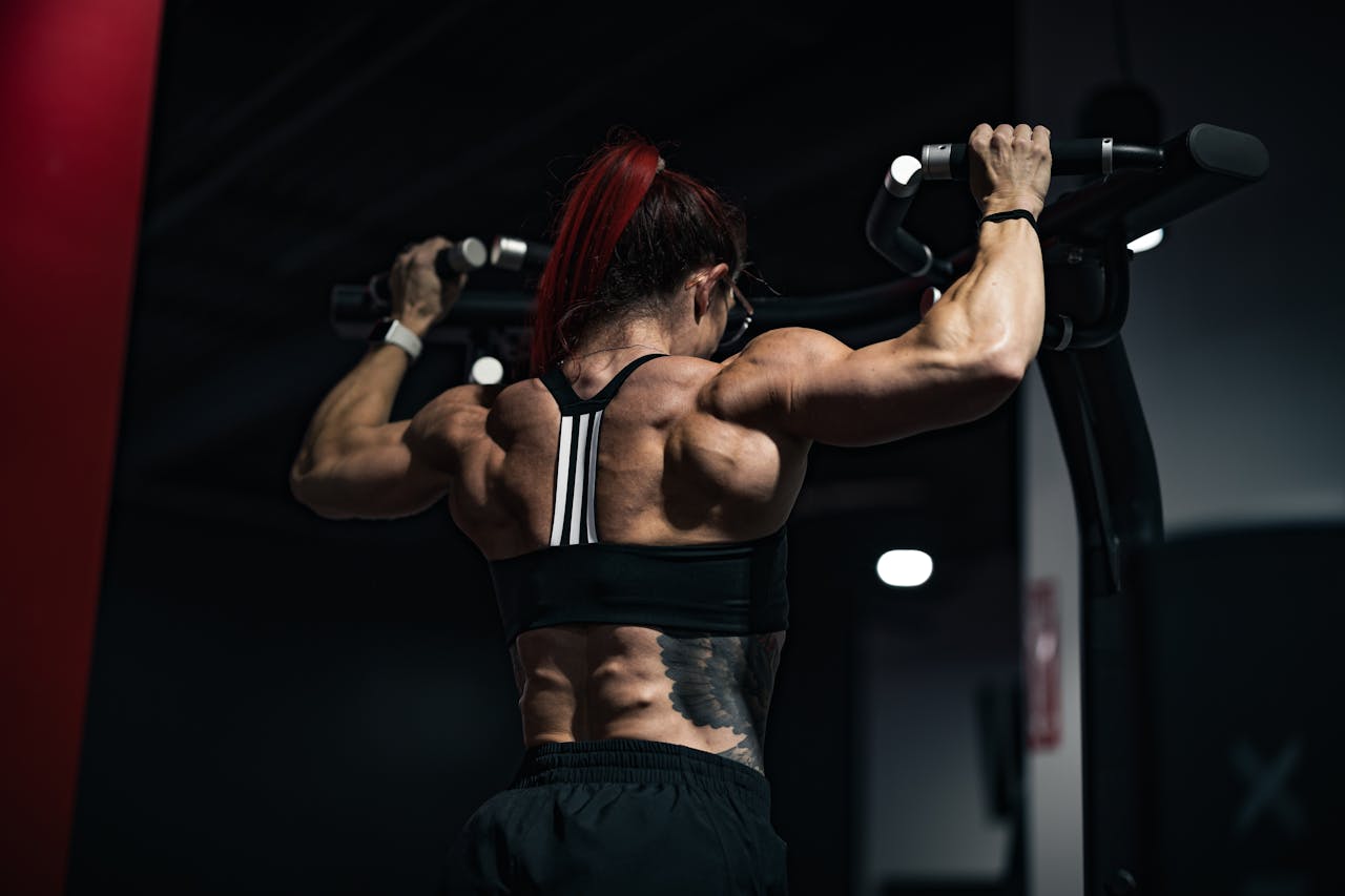 Back view of a muscular woman lifting weights in a gym, showcasing strength and determination.