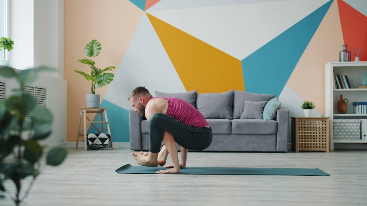 Adult man performing advanced yoga pose on a mat in a colorful and modern living room.